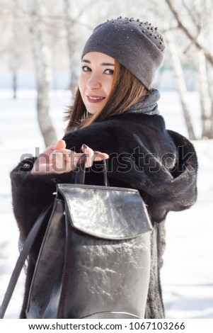 Beautiful girl in a black mink coat in the winter forest
