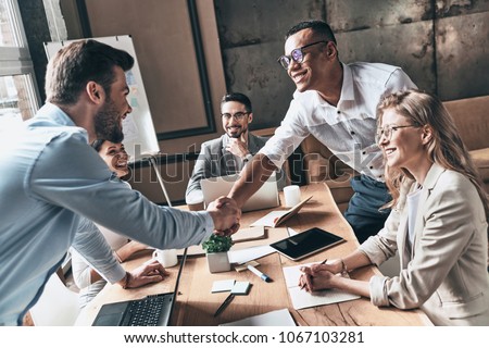 Welcome to our team! Top view of young modern men in smart casual wear shaking hands while working in the creative office Royalty-Free Stock Photo #1067103281