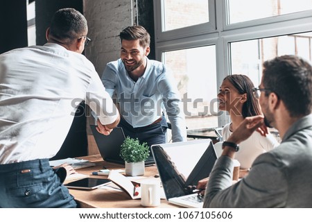 Glad to work with you! Young modern men in smart casual wear shaking hands and smiling while working in the creative office Royalty-Free Stock Photo #1067105606