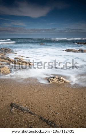 scenic atlantic coastline with waves in motion around rocks on sandy beach in long exposure, bidart, basque country, france