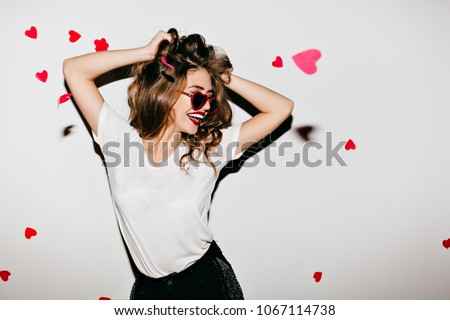 Slim european woman in glamorous sunglasses laughing on white background. Photo of good-looking girl playing with her wavy hair.