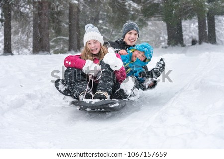 A group of kids/friends/family members tobogganing down a snow covered hill in a park.