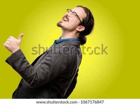 Handsome young man smiling broadly showing thumbs up gesture to camera, expression of like and approval