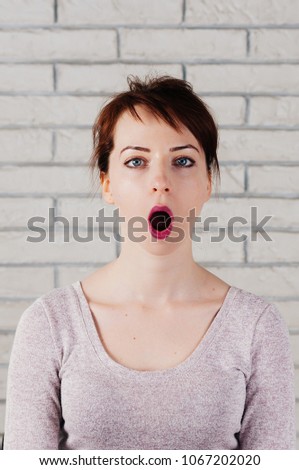A pretty girl with face mimic for fitness exercise, her mouth wide open, white brick wall in the background