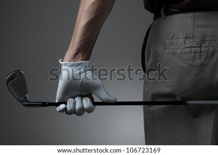 Closeup of a male golfer holding a six iron behind his body. Man has a Golf Glove on his hand. Horizontal format over a light to dark gray background.