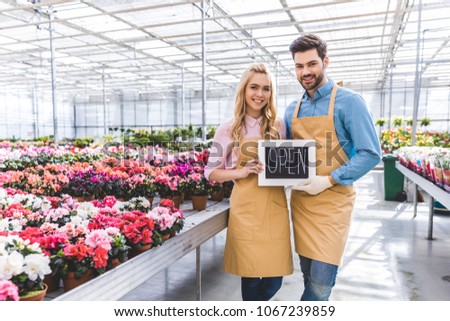 Male and female owners of glasshouse holding Open board by flowers