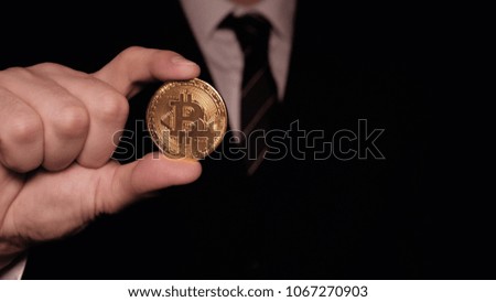 A businessman in a suit holds in his hand a gold bitcoin, a black background, a crypto currency, a course.