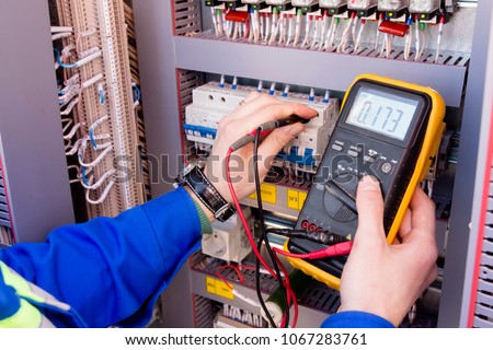 multimeter is in hands of engineer in electrical cabinet. Adjustment of automated control system for industrial equipment control cabinets. electrician measures voltage by tester Royalty-Free Stock Photo #1067283761