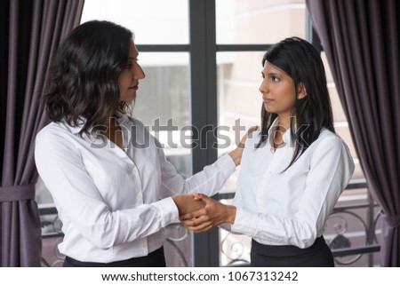 Content business woman supporting colleague in cafe. They are shaking hands and standing with window in background. Support concept. Side view.