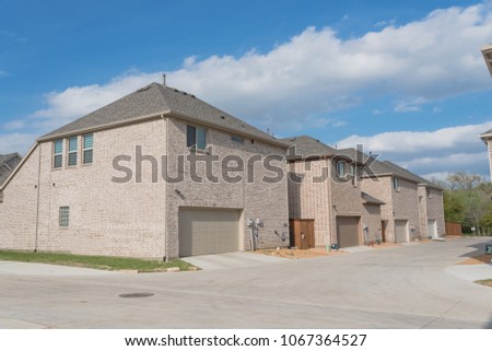 Typical rear entry garage of brand newly built house sold signs in Texas, USA. Row of detached lot garage in back, parking area behind new-established, unfinished landscape neighborhood. Blue sky