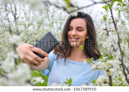 Girl make a selfie in blooming orchard. Beautiful woman enjoy in nature in spring