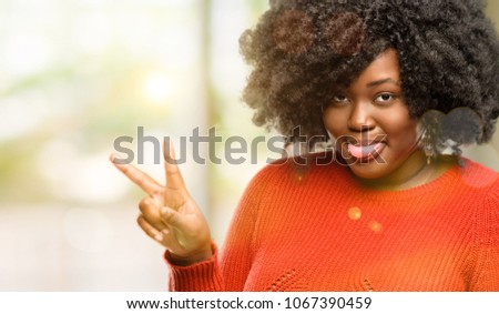 Beautiful african woman looking at camera showing tong and making victory sign with fingers, outdoor