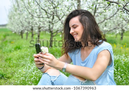 Girl texting on smartphone in a blooming orchid. Beautiful woman enjoy in nature in spring