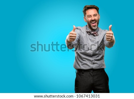 Middle age man, with beard and bow tie stand happy and positive with thumbs up approving with a big smile expressing okay gesture