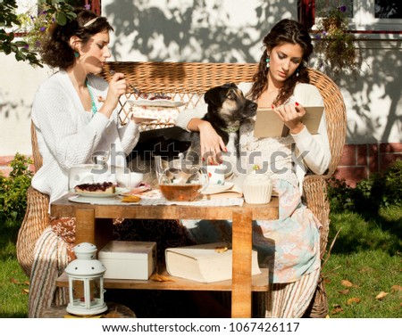 Two beautiful young women having a tea and cake in the garden