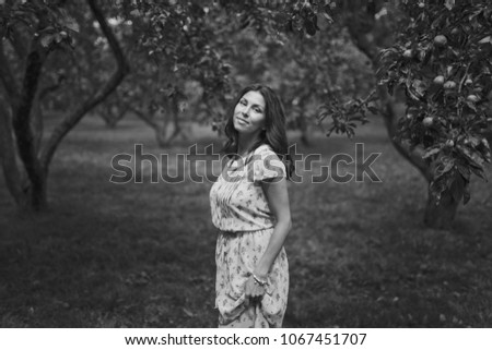 Beautiful smiling young brunette woman in a green summer garden amid the Apple trees with green fruit. Black and white photo.