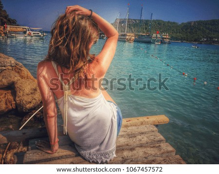 Girl seating on the wooden pier. Sea view, port, ships and boats. Mediterranean summer vibes.