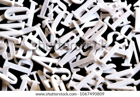 Heap of white plastic English alphabet letters casually kept on a plain black background. Used for display signs, education, name plates etc