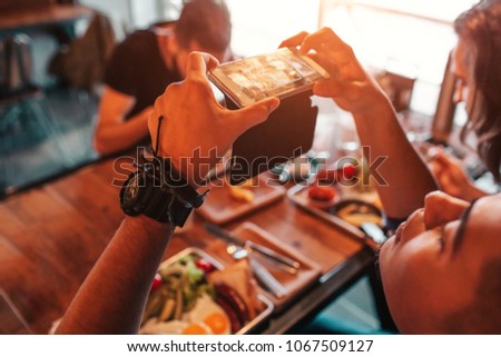 Young arabian man takes a picture of his breakfast on his phone for social network. Internet addiction concept. Friends having breakfast in bar.