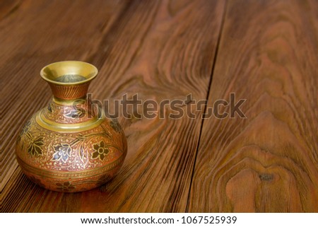 metal vase with an ornament on a wooden board