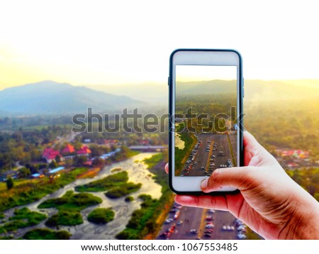 Hand holding smart phone and take a photo of landscape with cars park river mountain | blurred background and copy space on top