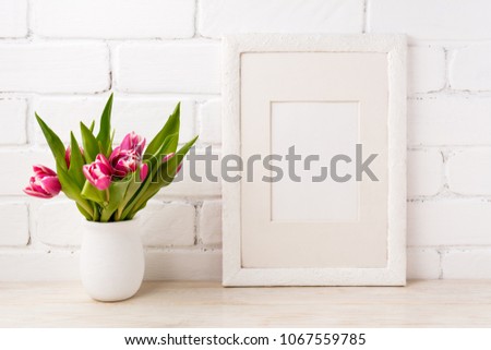 White frame mockup with bright magenta pink tulip bouquet in the flower pot. Empty frame mock up for presentation artwork. Template framing for modern art.