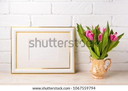 Gold decorated landscape, frame mockup with bright magenta pink tulip bouquet in the golden vase. Empty frame mock up for presentation artwork. Template framing for modern art.