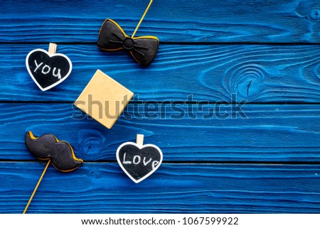 Gift for man on birthday. Gift box among cookies in shape of moustache, bow tie and hearts with lettering love you on blue wooden background top view copy space