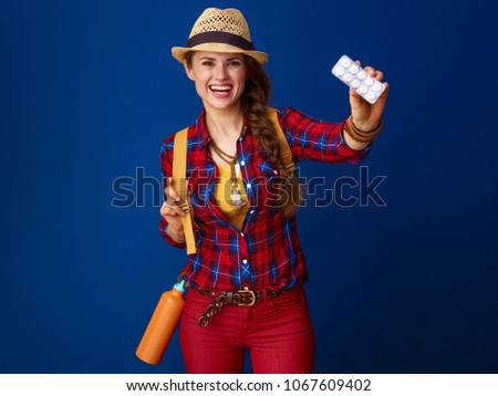 Searching for inspiring places. smiling active woman hiker with backpack showing tablets in a blister pack isolated on blue background