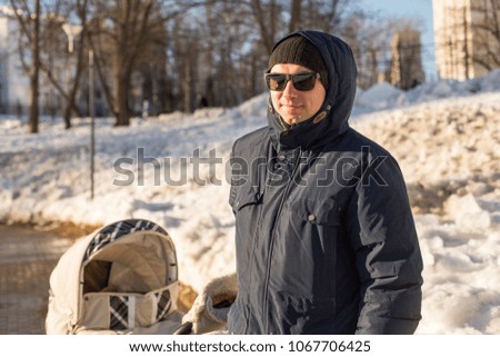 Dad walks with a baby in a baby carriage against the backdrop of a winter city