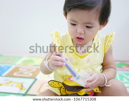 Selective focus of little Asian baby girl, 12 months old, playing with a syringe to get familiar with it - helping a baby reducing fear or a phobia of needles 