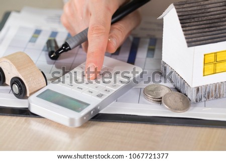 Young woman makes some calculations. Small paper house, coins, car in the background. Closeup