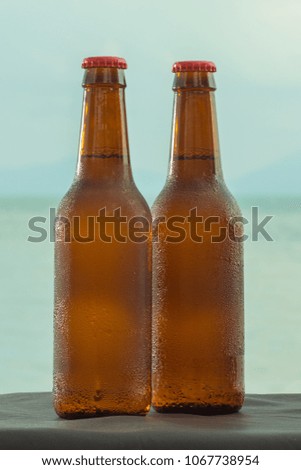 Brown beer bottles and blue sunglasses on a table on the background of the sea and sky