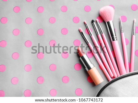 Cosmetic bag with different brushes of professional makeup artist and lipstick on color background