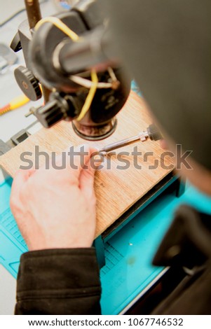 The engineer repairs the phone, the master solder the board, a soldering iron, a board, a working tool, a workshop, a man's hands, a telephone repair, a board, a light, a lamp, a phone repair macro