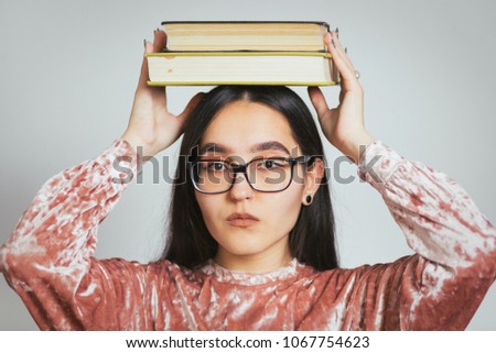 beautiful asian girl holding books on her head, wearing glasses and pink sweater, studio photo on background