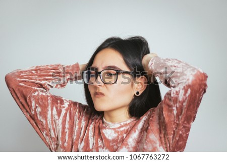 beautiful asian woman has a headache, wears glasses and a pink sweater, studio photo on the background