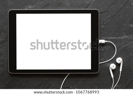 Tablet with empty screen and earphones on black stone surface