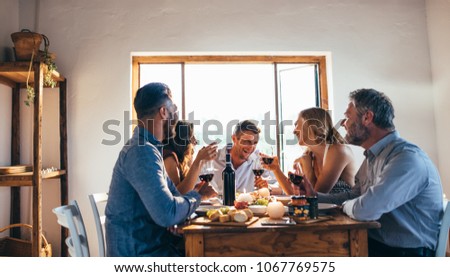 Young people got together by table with delicious food and glasses of red wine to celebrate a special occasion. Group of friends enjoying dinner party. Royalty-Free Stock Photo #1067769575