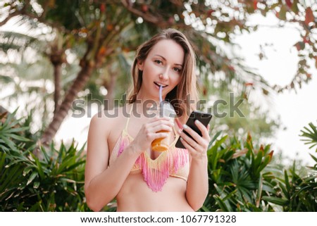 attractive girl drinking cocktail and holding smartphone at tropical resort