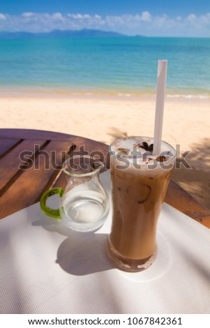 A glass of coffee with ice against the background of the sea and blue sky