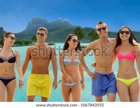summer holidays, travel and vacation concept - group of smiling friends wearing swimwear and sunglasses walking over exotic bora bora island background