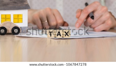 Word TAX composed of wooden letters. Female hand with a pen in the background. Closeup