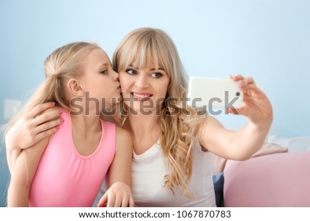 Cute little girl and her mother taking selfie at home
