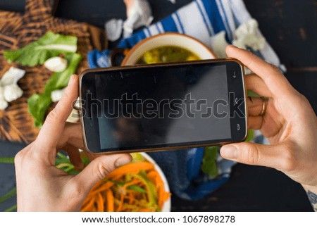 Woman hands take phone photo of vegetarian raw vegan dinner or lunch on table with lentil soup and vegetables salad. Social networks smartphone food photography.