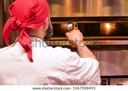 Professional pizza chef checks the temperature of his wood oven with a laser to cook gourmet pizza. Concept of: pizza, control, professional oven.