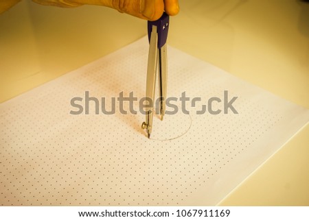 A hand drawing a perfect circle with a compass on a dotted paper.