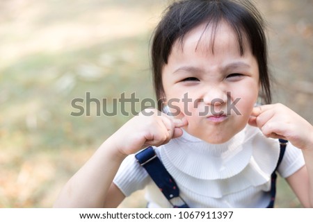 asian children travel in garden, she feeling happy and use her finger touch on her cheek