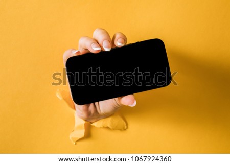 A woman holding a phone through a torn yellow paper Royalty-Free Stock Photo #1067924360