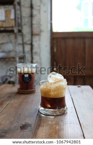 Iced bubbly shaken americano in curved short glass in a rustic wooden setting and natural light. 